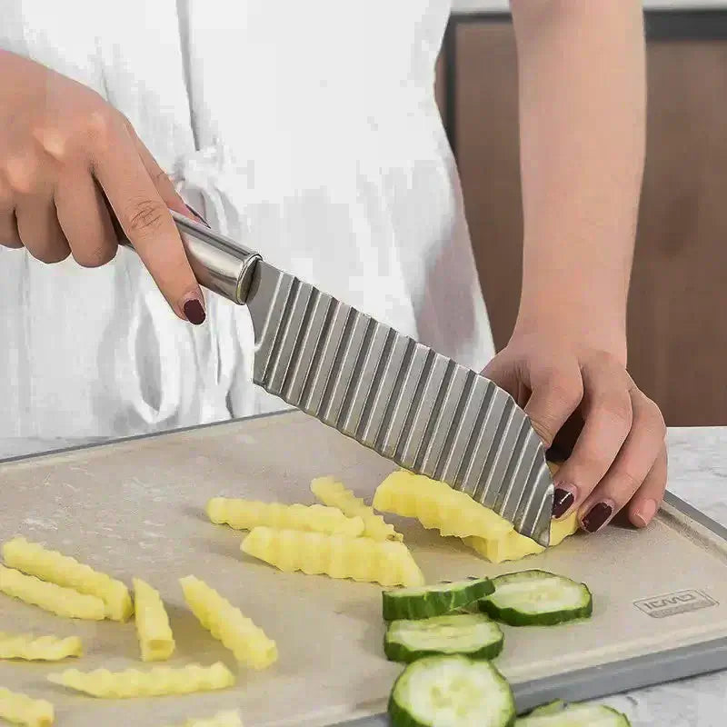 Une personne utilisant un couteau ondulé en inox pour découper des pommes de terre et des concombres en tranches et bâtonnets à motifs sur une planche à découper.