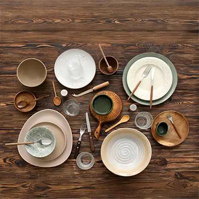 Ensemble de vaisselle en céramique et bois, comprenant des assiettes, bols, tasses, couverts et verres, disposés sur une table en bois. Idéal pour un service de table élégant et rustique.