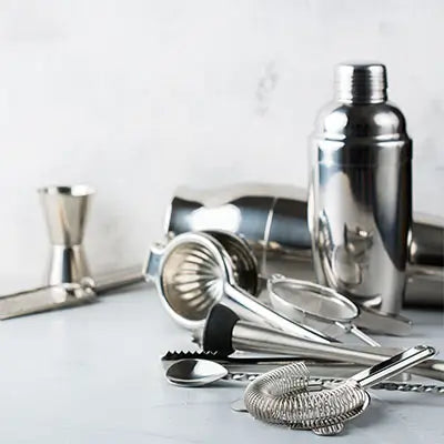 Ensemble d'ustensiles de bar en acier inoxydable incluant un shaker, une passoire, une cuillère à mélange, un jigger, un presse-agrumes et des pinces à glaçons. Parfait pour préparer des cocktails.