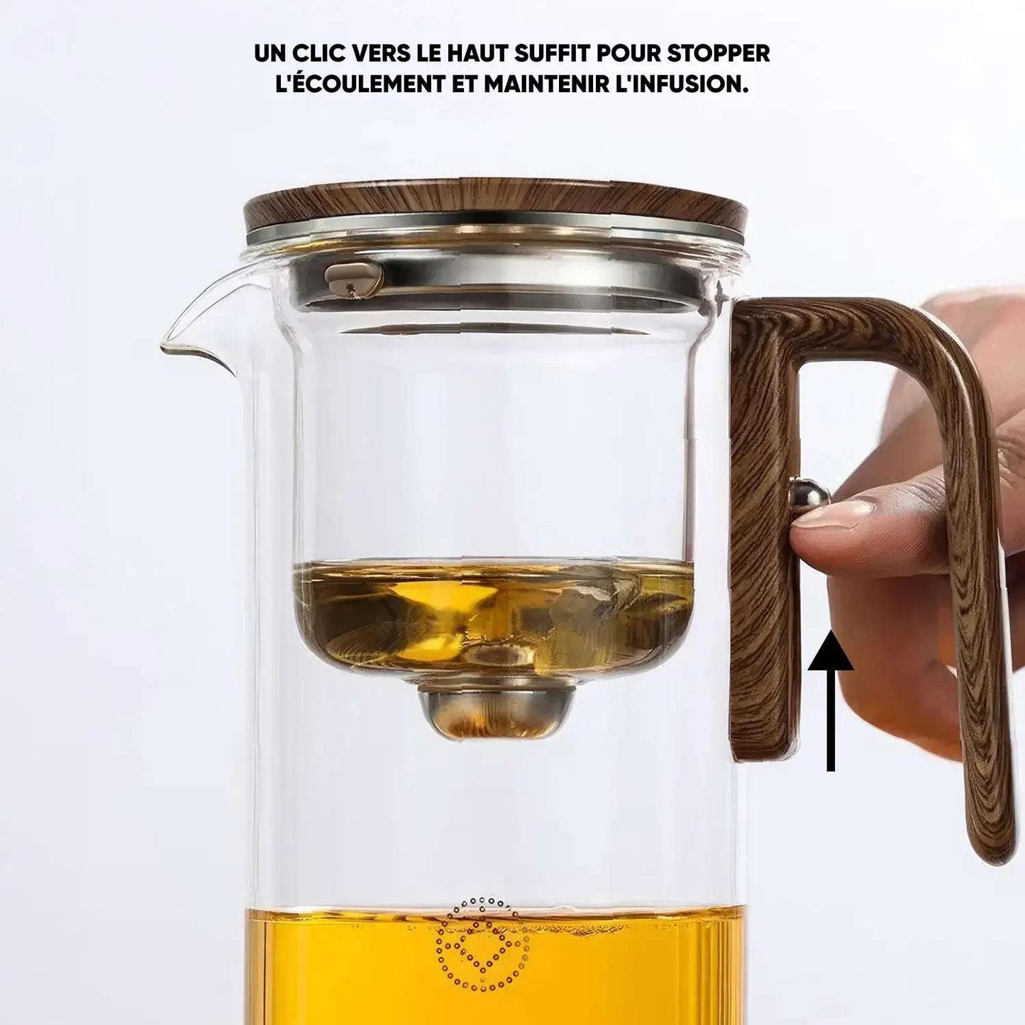 Théière en verre avec infuseur intégré, montrant une main actionnant le bouton sur la poignée pour stopper l'écoulement du thé.