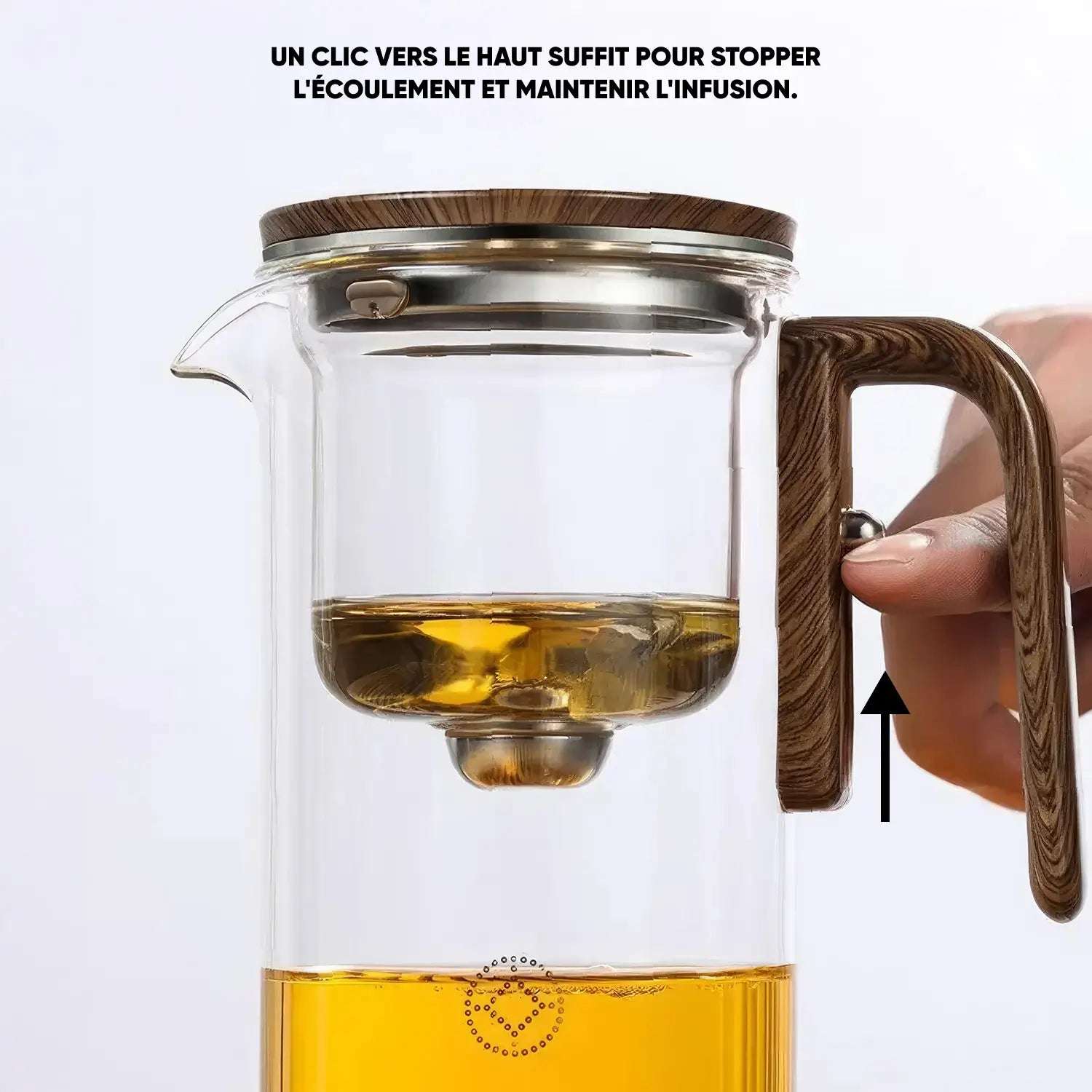 Théière en verre avec infuseur intégré, montrant une main actionnant le bouton sur la poignée pour stopper l'écoulement du thé.