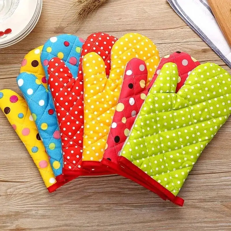 Ensemble de gants de cuisine matelassés avec différents coloris et motifs à pois, alignés sur une table en bois.