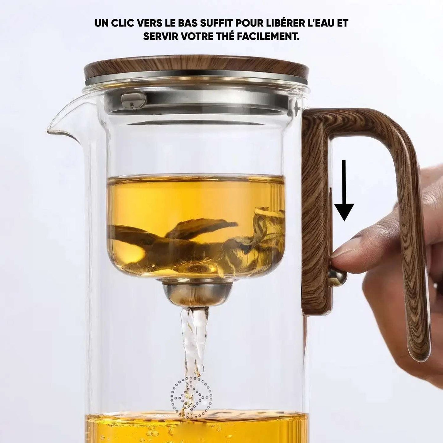 Théière en verre remplie de thé, avec une main appuyant sur un bouton de la poignée pour libérer le thé dans la partie inférieure.