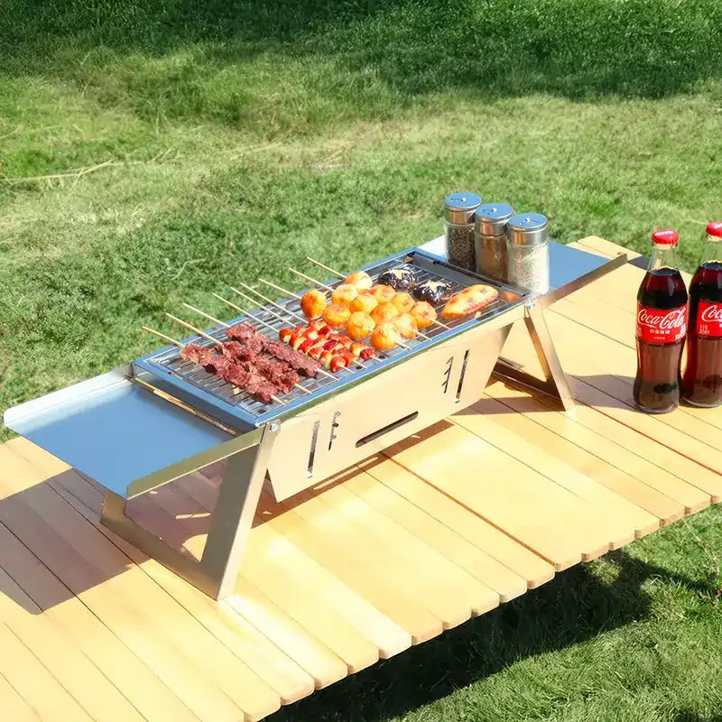 Mini barbecue portable inox en pleine utilisation avec brochettes et épices sur table de jardin