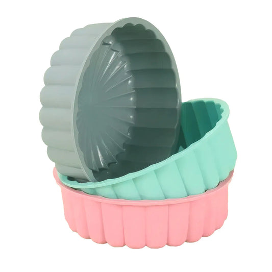 Trois moules à charlotte en silicone empilés, de différentes couleurs : gris, vert menthe, et rose. Les moules sont de forme ronde avec des bords ondulés.