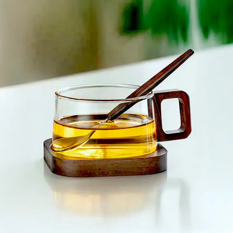 Tasse à café en verre borosilicate transparent avec liquide ambré, poignée et cuillère en bois sur un socle en bois