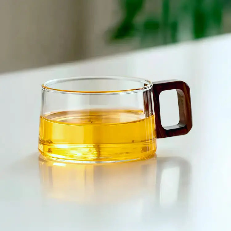 Tasse à café en verre borosilicate transparent contenant un liquide ambré avec poignée en bois