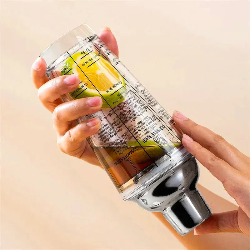 Shaker à cocktail tenu à la main, montrant des morceaux de citron et un liquide, avec des instructions de recette imprimées sur la surface en verre.